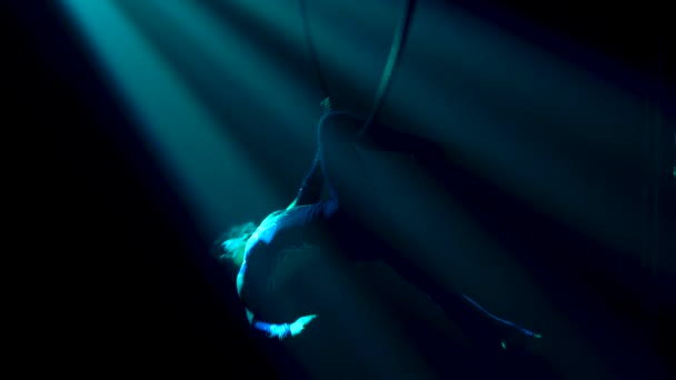 Graceful performance of the flexible female artist of the circus on the air ring under the dome. Silhouette of a slim body in a tight fitting suit in magical rays of light. Close up. — Stock Video