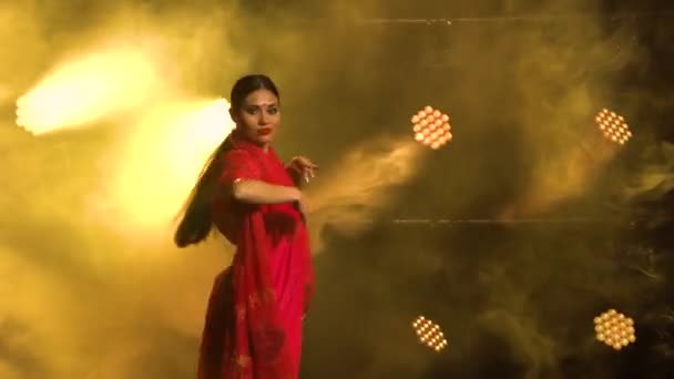 Una giovane ballerina in un sari rosso. Danza popolare indiana. Girato in uno studio buio con fumo e illuminazione al neon gialla. — Video Stock