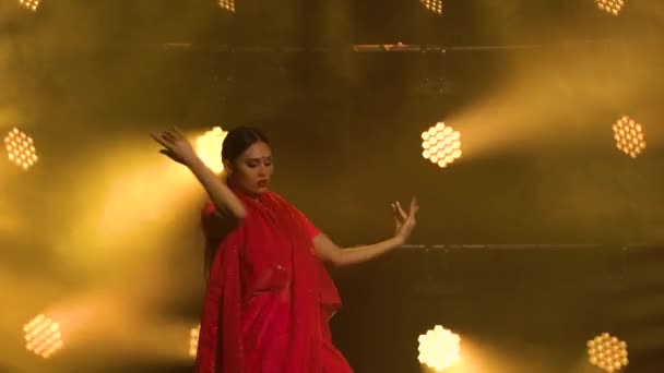 Una giovane ballerina in un sari rosso. Danza popolare indiana. Girato in uno studio buio con fumo e illuminazione al neon gialla. — Video Stock