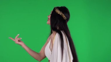 Yunan tanrısı elbisesi ve yüksek çelenk modayla güzel bir kadının portresi cilveli bir şekilde gülümsemek, el sallamak ve el sallayarak buraya gelmektir. Yan görüş. Yeşil Ekran.