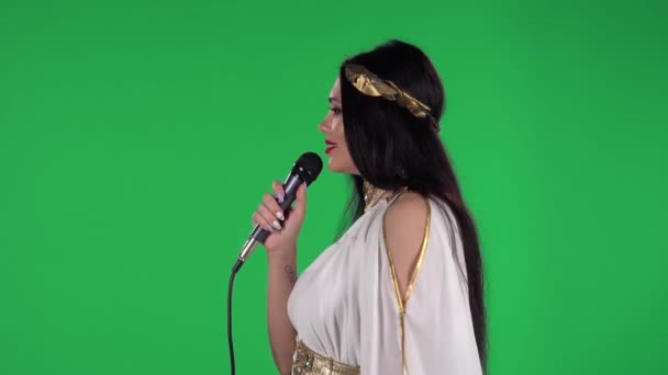 Πορτρέτο της όμορφης γυναίκας στο ελληνικό φόρεμα greece goddes και στεφάνι υψηλής μόδας κοιτάζει ευθεία και τραγουδά στο μικρόφωνο. Πράσινη οθόνη. Πλευρική άποψη. — Αρχείο Βίντεο