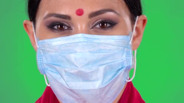 Egy gyönyörű indiai nő portréja védő orvosi maszkban, ahogy a kamerába néz. Zöld vászon. Közelről. Makrofényképezés. — Stock videók