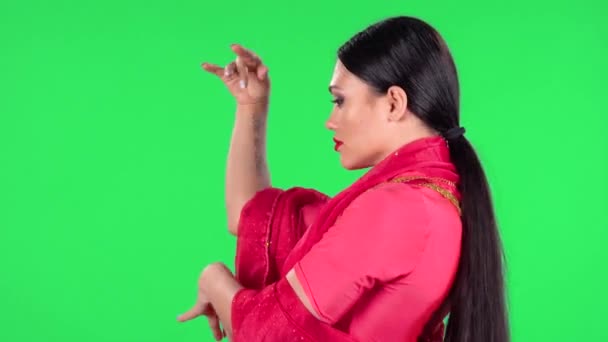 Porträtt av en ung indisk kvinna i nationell klassisk röd sari ser rakt ut och dansar. Sidovy. Grön skärm. — Stockvideo