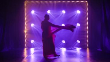 Siluet kırmızı sarili genç bir kız dansçı. Hint halk dansı. Duman ve neon ışıkla karanlık bir stüdyoda çekildi. Yavaş çekim.