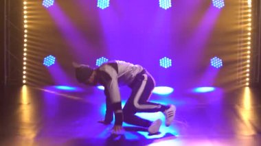 Erkek dansçı break dans, hip hop, stüdyoda sokak dansı, izole. Genç bir adam mor ışıklandırmalı karanlık bir stüdyoda break dans yapıyor. Kapat..