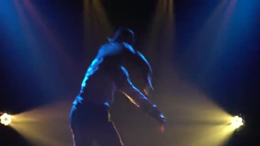 Dumanlı arka planda dans eden yakışıklı bir adam silueti, günlük giysiler giyiyor, sokak dansı yapıyor. Kapat..