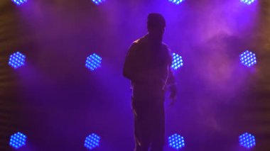 Bir erkek dansçının silueti break dans, hip hop, stüdyoda sokak dansı, izole. Genç adam mor ışıklandırmalı karanlık bir stüdyoda break dans yapıyor. Kapat..