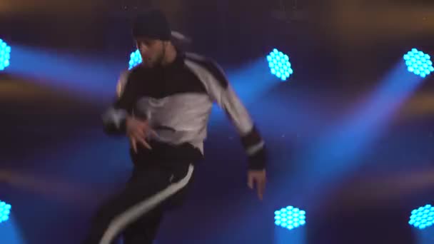 Un joven talentoso haciendo movimientos de baile de frenos de cerca. Bailarina masculina en ropa de calle realiza contra el telón de fondo de las luces azules del estudio. — Vídeos de Stock