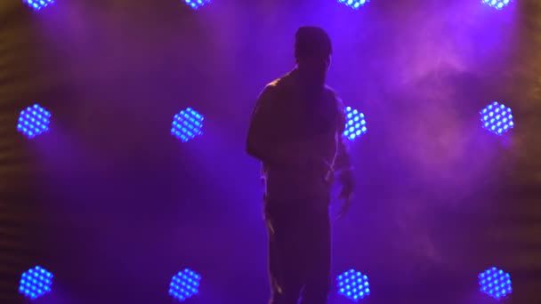 Silhouette egy férfi táncos break dance, hip hop, utcai tánc a stúdióban, elszigetelt. A fiatalember breakdance elemeket ad elő egy sötét stúdióban, lila háttérvilágítással. Közelről.. — Stock videók