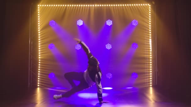 Elementos complexos de breakdance realizados por um dançarino profissional em um estúdio escuro cercado por luzes de néon. Movimento lento. — Vídeo de Stock
