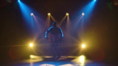 Breakdance 'in profesyonel performansı, stil sahibi bir sokak dansçısı tarafından sahnelenen hip hop. Eşofmanlı ve spor ayakkabılı bir adamın silueti sahne ışıklarının arka planında. Yavaş çekim.