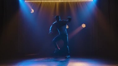 Breakdance 'in profesyonel performansı, stil sahibi bir sokak dansçısı tarafından sahnelenen hip hop. Eşofmanlı ve spor ayakkabılı bir adamın silueti sahne ışıklarının arka planında. Yavaş çekim.
