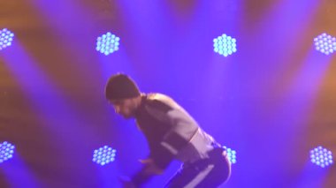Erkek dansçı break dans, hip hop, stüdyoda sokak dansı, izole. Genç bir adam mor ışıklandırmalı karanlık bir stüdyoda break dans yapıyor. Kapatın. Yavaş çekim.