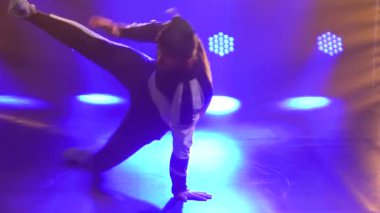 Erkek dansçı break dans, hip hop, stüdyoda sokak dansı, izole. Genç bir adam mor ışıklandırmalı karanlık bir stüdyoda break dans yapıyor. Kapatın. Yavaş çekim.