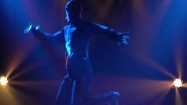 Karanlık bir stüdyoda sahne ışığında break dans yapan genç bir adamın siluetleri. Kapatın. Yavaş çekim.