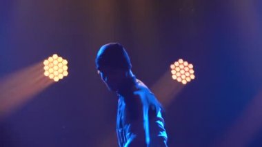 Karanlık bir stüdyoda sahne ışığında break dans yapan genç bir adamın siluetleri. Kapatın. Yavaş çekim.