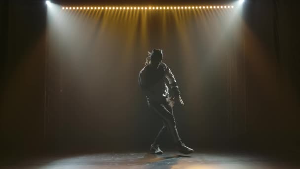 Banbrytande rörelser i en mörk ateljé under strålkastarna. Silhuetter av en dansande man i slow motion. — Stockvideo