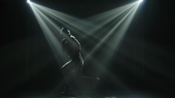 Breakdancebewegingen in een donkere studio onder de schijnwerpers. Silhouetten van een dansende man in slow motion. — Stockvideo