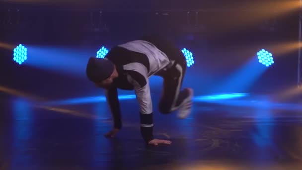 Mladý talentovaný muž dělá pohyby při brždění zblízka. Mužský tanečník v streetwear vystupuje na pozadí studiových modrých světel. Zpomalený pohyb. — Stock video