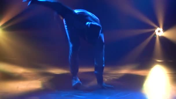 Siluety mladého muže, jak cvičí breakdance v tmavém studiu ve světle reflektorů. Zavřít. Zpomalený pohyb. — Stock video