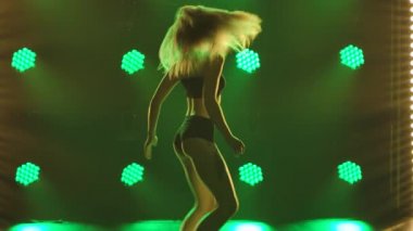 Kadın dansçı, popo dansı yapan bir twerk 'i sallıyor. Dans eden güzel kadınlar. Spot ışıklarının yeşil ışıklarında yarı çıplak bir vücudun silueti. Kapatın. Yavaş çekim.