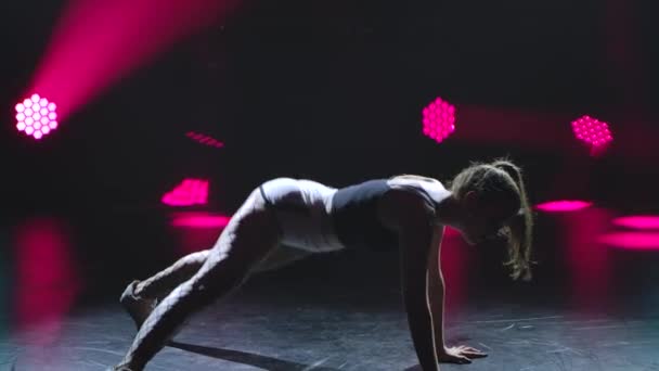 Flexible woman moving her ass dancing twerk in shorts on a black background with crimson lights. Silhouette. Close up. Slow motion. — Vídeos de Stock