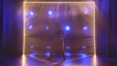 Attractive woman sexy moving her torso and ass dancing twerk in studio. Silhouette against the background of blue lights. Slow motion.