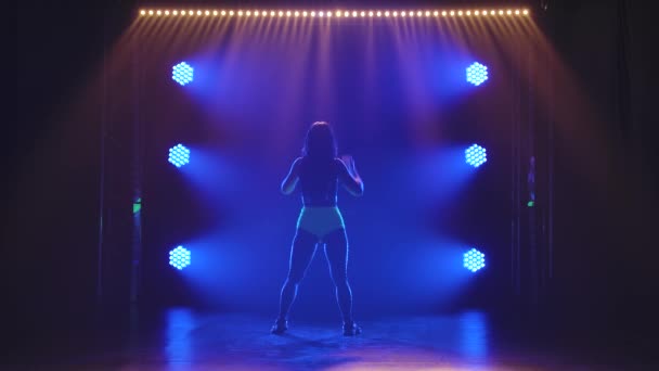 Attractive woman sexy moving her torso and ass dancing twerk in studio. Silhouette against the background of blue lights. Slow motion. — Vídeo de stock