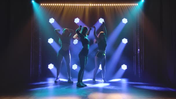 Three sensual long haired woman shaking her ass dancing twerk in studio against a background of blue lights. Silhouette. Slow motion. — Vídeo de Stock