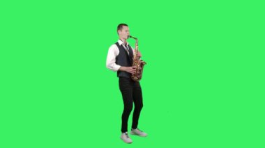 Portre stili genç adam stüdyodaki yeşil ekranda saksafonda melodi çalıyor. Saxophonist solo performans sergiliyor. Yan görünüm.