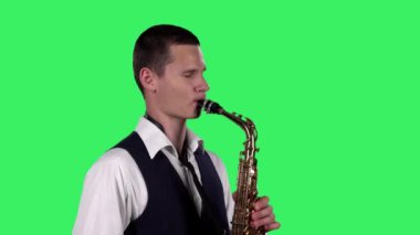 Portre stili genç adam stüdyodaki yeşil ekranda saksafonda melodi çalıyor. Saxophonist solo performans sergiliyor. Kapatın. Yan görünüm.