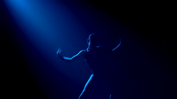 Sylwetka młoda elastyczna baletnica w czarnym body z wdziękiem tańcząca w ciemności pod teatralnymi niebieskimi reflektorami pracowni. — Wideo stockowe