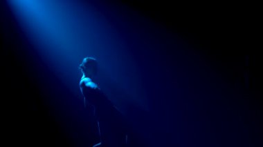 Siluet. Siyah elbiseli, esnek bir balerin. Stüdyonun mavi sahne ışıkları altında karanlıkta zarif bir şekilde dans ediyor..