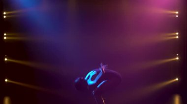 Siyahlar içinde profesyonel bir balerin. Dinamik spot ışıkları altında zarif bir şekilde bale yapıyor ve sahnede sigara içiyor. Güzel, ince bir siluetin silueti.