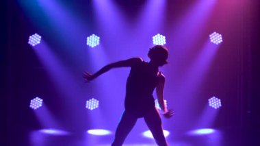 Siluet. Siyah elbiseli, esnek bir balerin. Stüdyonun mavi sahne ışıkları altında karanlıkta zarif bir şekilde dans ediyor..