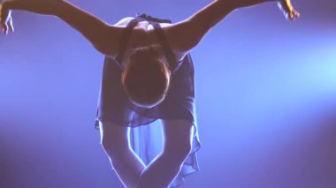 Profesyonel balerin sahne ışıkları altında bale yapıyor ve sahnede sigara içiyor. Güzel, ince bir siluetin silueti. Kapat..