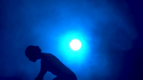 Silhouette egy fiatal rugalmas balerina fekete testöltözékben kecses tánc a sötétben egy színpadi kék reflektorfényben stúdió. — Stock videók