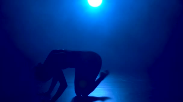 Silhouette egy fiatal rugalmas balerina fekete testöltözékben kecses tánc a sötétben egy színpadi kék reflektorfényben stúdió. — Stock videók