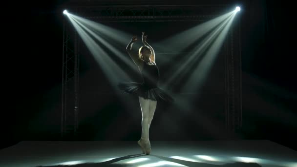 Silhouette a ballerina in black tutu and pointe ballet shoes. Graceful dancing of elements classical ballet. Shot in a darkness under a theatrical spotlights on black background. Slow motion. — Stock Video