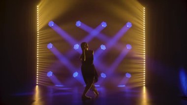 Profesyonel balerin sahne ışıkları altında bale yapıyor ve sahnede sigara içiyor. Güzel, ince bir siluetin silueti. Yavaş çekim.