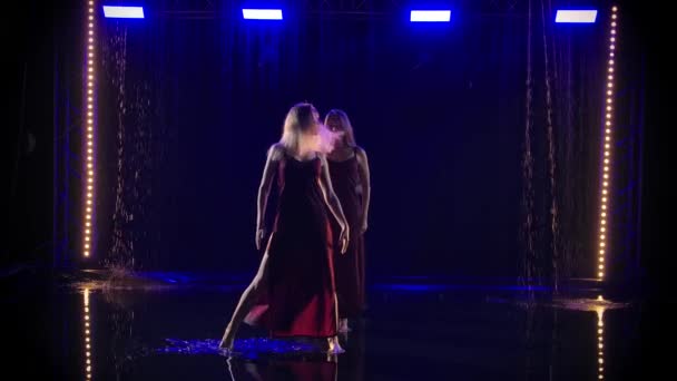 Trois danseuses élancées dansent gracieusement à travers les flaques d'eau de pluie sur fond de gouttes d'eau tombantes. Mouvement lent. — Video