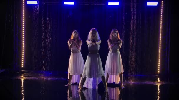 Tres hermosas mujeres jóvenes con rozvmi en sus manos están bailando sobre un fondo de lluvia y luz azul. Movimiento lento. — Vídeos de Stock