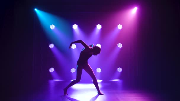 ブラックボディスーツのプロのバレリーナは、ダイナミックなスポットライトとステージ上の煙で優雅にバレエを踊ります。美しいスリムな姿のシルエット。スローモーション. — ストック動画