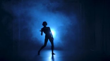 Stüdyonun mavi sahne ışıkları altında karanlıkta esnek dans edebilen siyah elbiseli profesyonel bir balerin. Yavaş çekim.