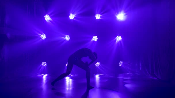 Siyahlar içinde profesyonel bir balerin. Dinamik spot ışıkları altında zarif bir şekilde bale yapıyor ve sahnede sigara içiyor. Güzel, ince bir siluetin silueti. Yavaş çekim. — Stok video