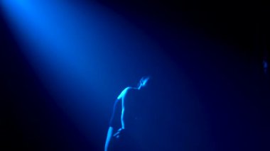 Siluet, siyah takım elbiseli, esnek, genç bir balerin zarif bir dans. Stüdyonun mavi sahne ışıkları altında karanlıkta çekildi. Yavaş çekim.