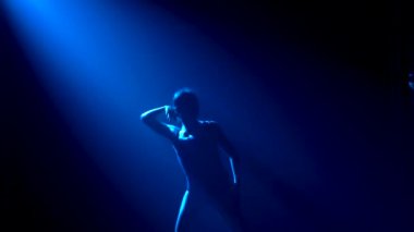 Siluet, siyah takım elbiseli, esnek, genç bir balerin zarif bir dans. Stüdyonun mavi sahne ışıkları altında karanlıkta çekildi. Yavaş çekim.