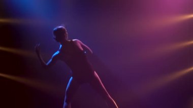 Siyah elbiseli profesyonel balerin zarif bir şekilde bale yapıyor. Dinamik spot ışıklarında ve sahnede dumanla çekilen. Güzel, ince bir siluetin silueti. Yavaş çekim.