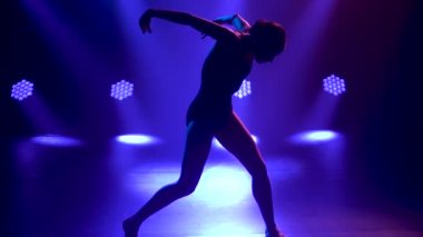 Siyah elbiseli profesyonel balerin zarif bir şekilde bale yapıyor. Dinamik spot ışıklarında ve sahnede dumanla çekilen. Güzel, ince bir siluetin silueti. Yavaş çekim.