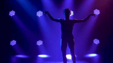 Siyah elbiseli profesyonel balerin zarif bir şekilde bale yapıyor. Dinamik spot ışıklarında ve sahnede dumanla çekilen. Güzel, ince bir siluetin silueti. Yavaş çekim.